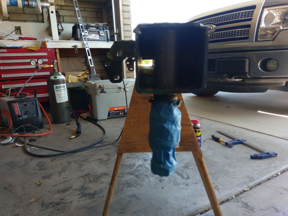 Part of a vehicle frame on a stand, with a silver truck grille visible behind