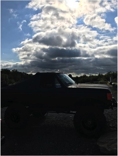 1989 Ford Bronco - A black 1989 Ford Bronco is silhouetted against a dramatic sky with heavy clouds.