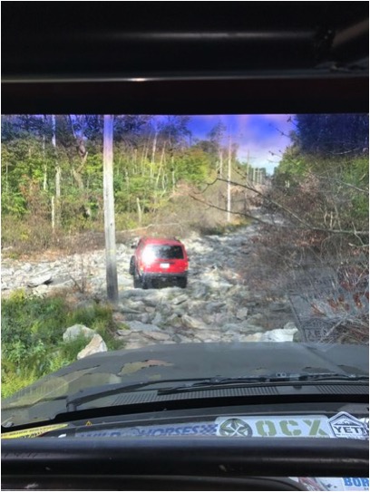 1989 Ford Bronco - A red SUV navigates a challenging, rocky off-road path through a wooded area.