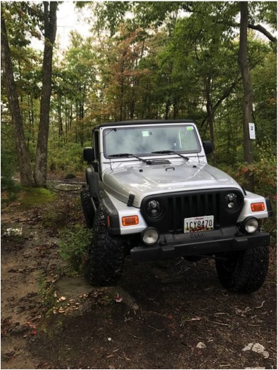 1989 Ford Bronco - A silver Jeep Wrangler navigates a rocky, wooded trail.
