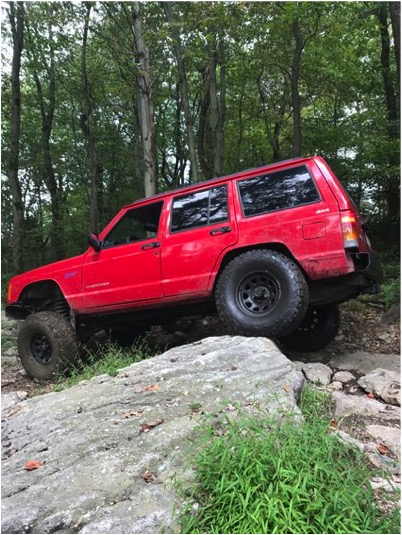 1989 Ford Bronco - A red Jeep Cherokee navigates a rocky trail with tall trees surrounding it.