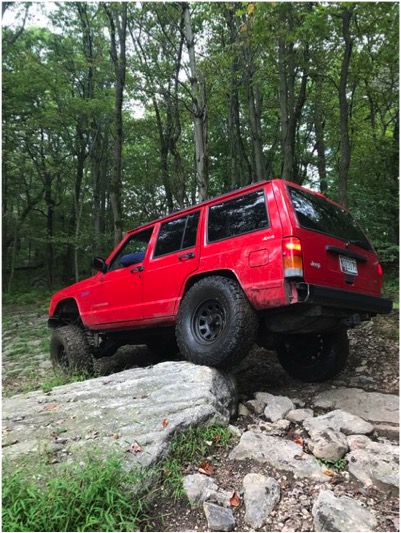1989 Ford Bronco - A red Jeep Cherokee navigates rocky terrain, its body style indicating it is likely a 1984 model.