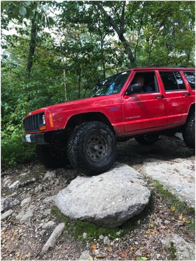 1989 Ford Bronco - A red Jeep Cherokee navigates a challenging rocky terrain off-road.