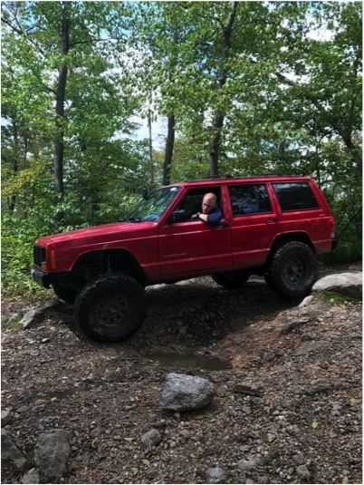 1989 Ford Bronco - Driver in a red Jeep Cherokee XJ navigates a rough, wooded path.