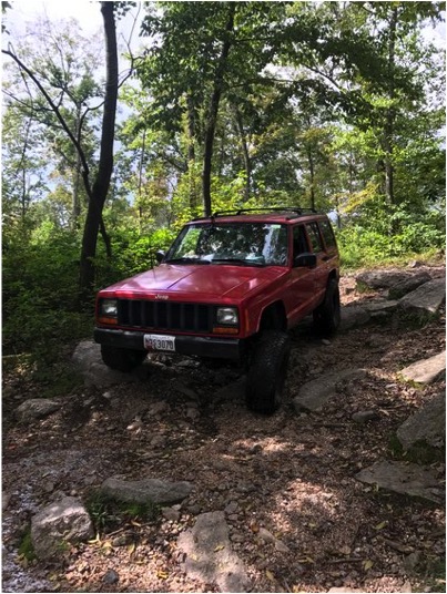 1989 Ford Bronco - A red Jeep Cherokee XJ navigates a rocky path through a wooded area.