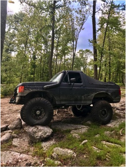 1989 Ford Bronco - This modified Ford Bronco is navigating a rocky trail through a wooded area.