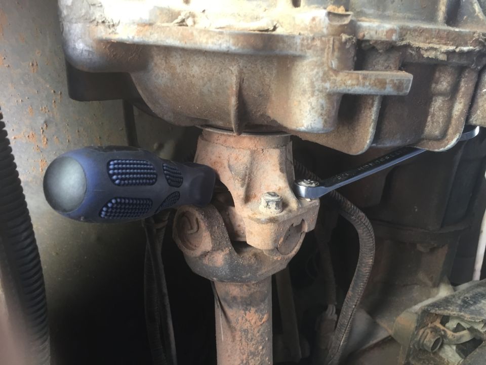Drivetrain components with a screwdriver and wrench, showing a universal joint and part of a transmission housing