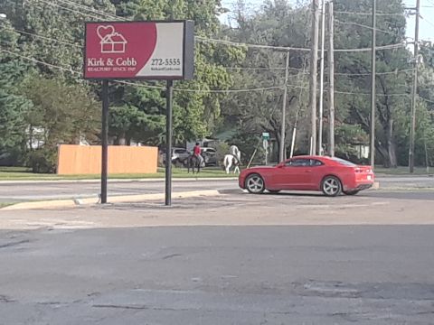 1994 Ford Bronco - Red sports car seen on street next to Kirk & Cobb Realty sign with horses in background.