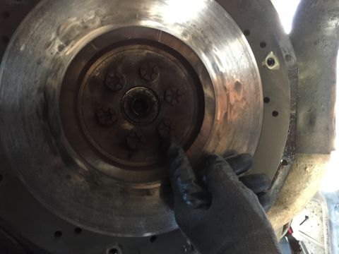 1986 Ford Bronco - A gloved hand inspects the bolts on a greasy flywheel, part of a vehicle's clutch assembly.