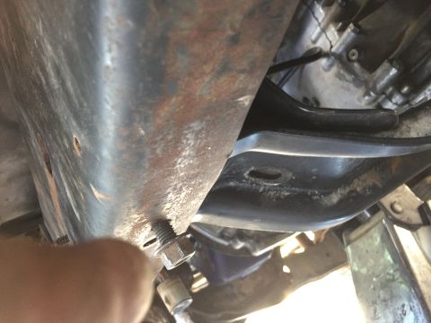 1986 Ford Bronco - A mechanic works on a bolt and nut assembly on the underside of a vehicle, likely during a repair or modification.