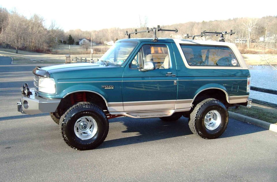 Teal and tan lifted Ford Bronco SUV, driver's side view, parked near water