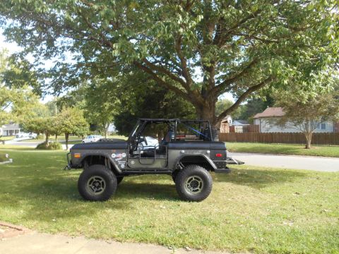 1972 Ford Bronco - This modified 1972 Ford Bronco features a roll cage and large off-road tires, parked on a residential lawn.