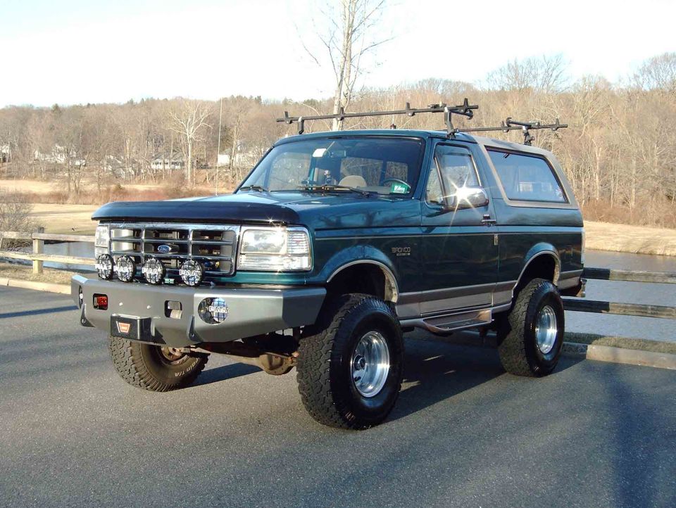 Dark green lifted Ford Bronco SUV with white top, front-left view, on paved lot