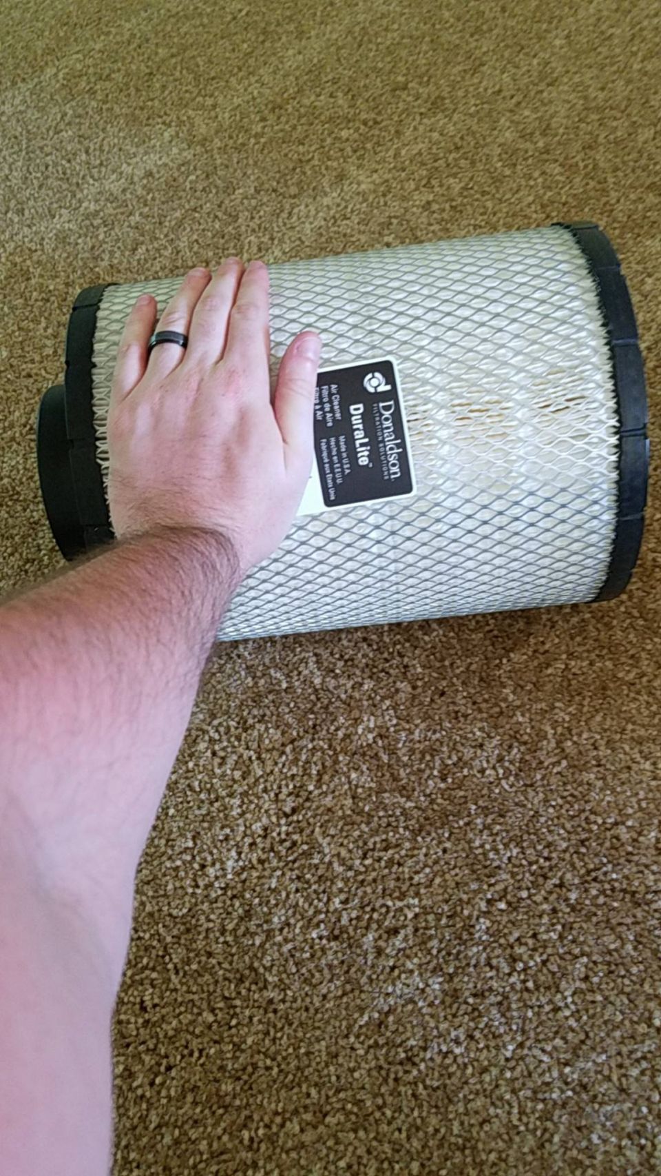 Hand resting on a large white Donaldson DuraLite air filter element lying on tan carpet