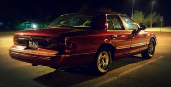1995 Mercury Grand Marquis - A maroon 1995 Mercury Grand Marquis sedan is parked in a lot at night, viewed from the rear three-quarter angle.