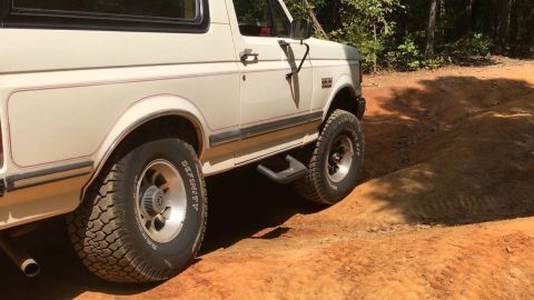 1988 Ford Bronco - White 1988 Ford Bronco navigating a dirt path with trees in the background.