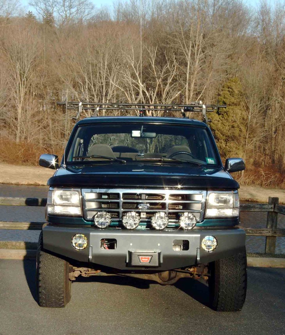 Dark green Ford SUV front end with WARN winch bumper and four PIAA lights on grille.