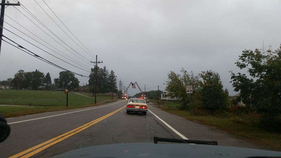 Car driving down a wet road, passing a fire truck with an American flag