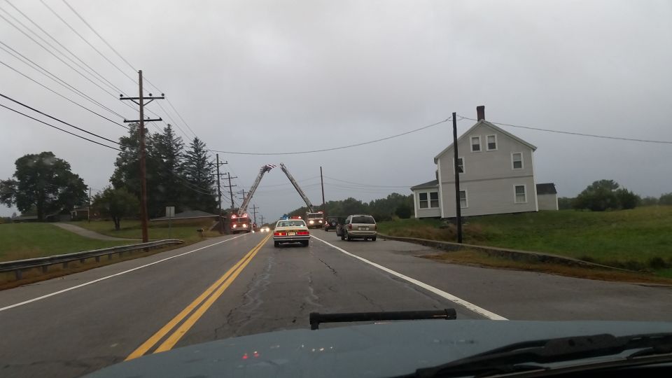Two fire trucks with extended ladders, a sedan, and a van on a wet road near a house