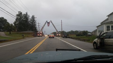1991 Ford Crown Victoria - Fire trucks form an arch with an American flag over a road during what appears to be a ceremony.
