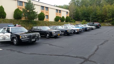 1991 Ford Crown Victoria - A row of police vehicles, including a black and white patrol car, are parked in a lot outside a motel.