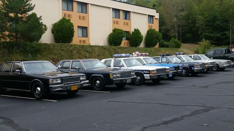 1991 Ford Crown Victoria - Several police vehicles are lined up in a parking lot, with a motel in the background.