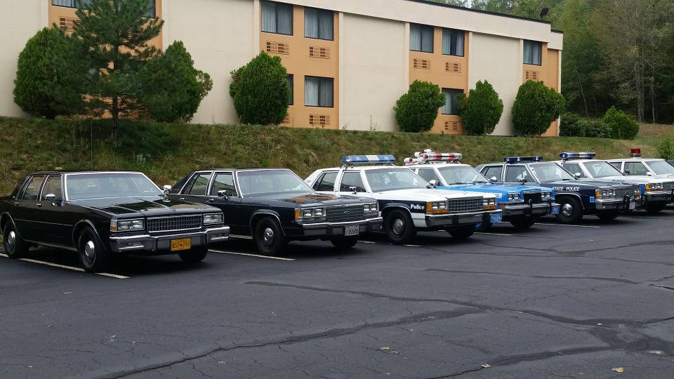 Row of police cars, including a black unmarked sedan and several marked units