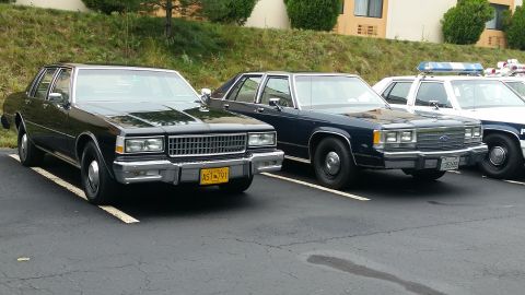 1991 Ford LTD Crown Victoria - Two older model police sedans are parked side-by-side in a parking lot.