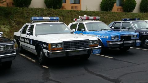 1991 Ford LTD Crown Victoria - Several police cars are parked in a lot, including a white Boston Police car and a blue police car.