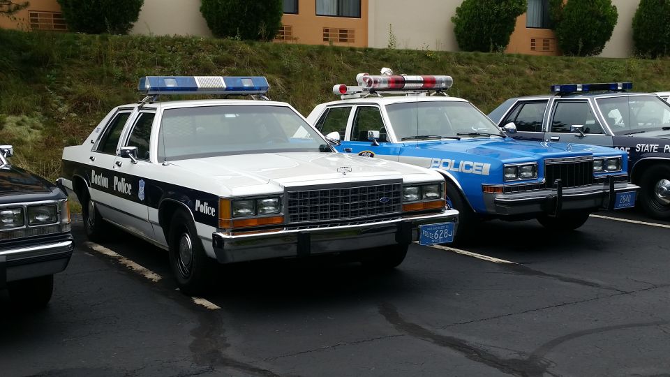 White police car with "Boston Police" text, parked next to a blue police car