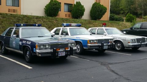 1991 Ford LTD Crown Victoria - Three police sedans are parked in a lot, two of which are equipped with light bars.