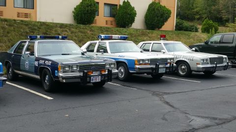 1991 Ford LTD Crown Victoria - Three police sedans are parked in a lot, showing different markings and light bars.