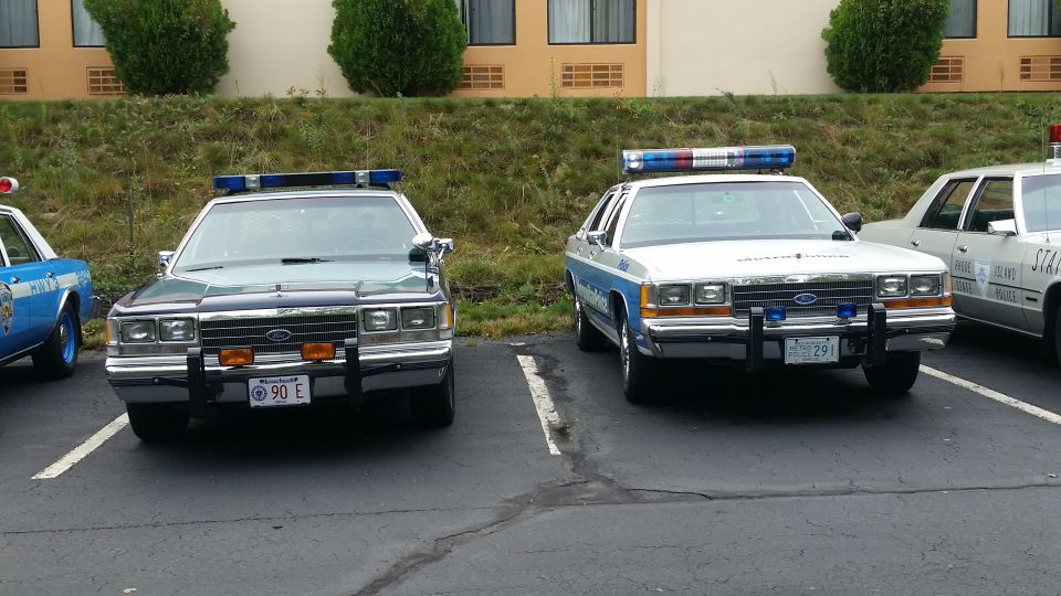 Two police cars parked, one dark green and one white with blue stripes. Both have light bars