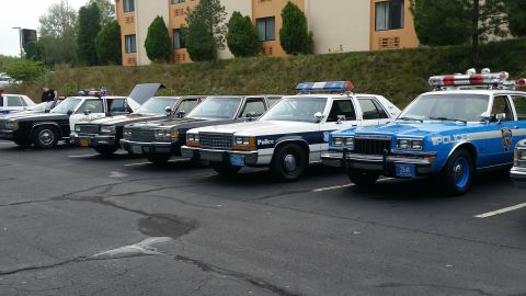 1991 Ford LTD Crown Victoria - Several police cars are parked in a lot, including a blue and white vehicle with "POLICE" visible on the door.