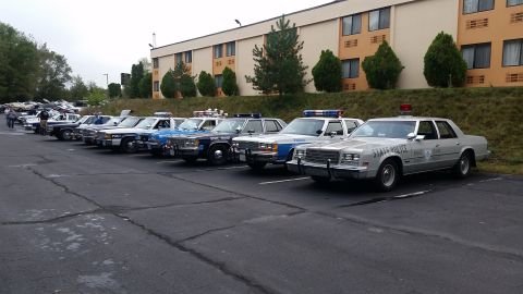 1991 Ford LTD Crown Victoria - A lineup of older model police cruisers are parked in a lot outside a motel.