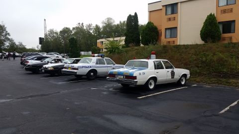 1991 Ford LTD Crown Victoria - Several police cars are parked in a lot next to a building.