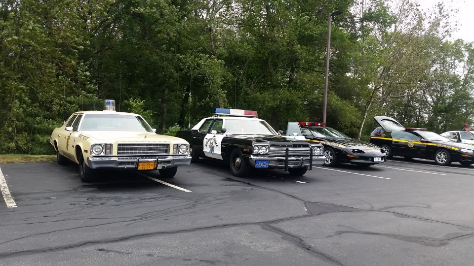 Front view of a cream-colored police car with a light bar, parked next to other police vehicles