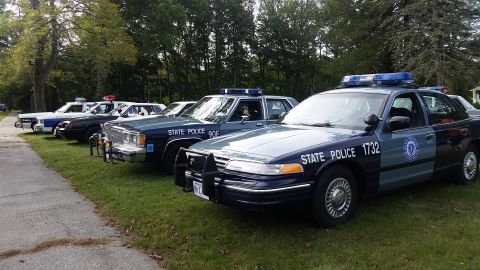 1991 Ford LTD Crown Victoria - A line of state police vehicles, including a 1991 Ford Crown Victoria, are parked on a grassy area.