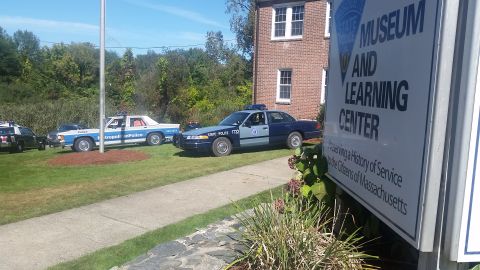 1991 Ford LTD Crown Victoria - Police cars are parked on the lawn outside a museum and learning center.
