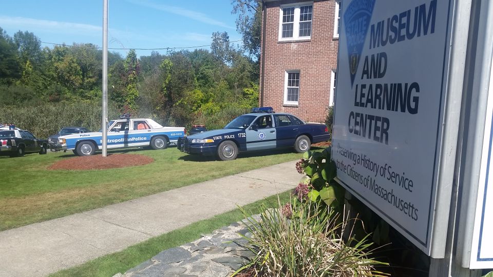 Two police cars parked on grass in front of a brick building with a sign that reads 'MUSEUM AND LEARNING CENTER'