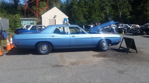 1991 Ford LTD Crown Victoria - Light blue police car from the 1970s with its hood up, parked outdoors with other vehicles.