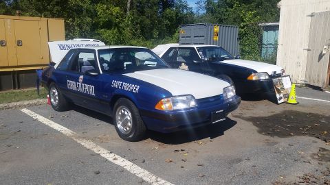 1991 Ford LTD Crown Victoria - Two Ford Mustangs, one marked as Georgia State Patrol, are parked outdoors near a generator and storage containers.