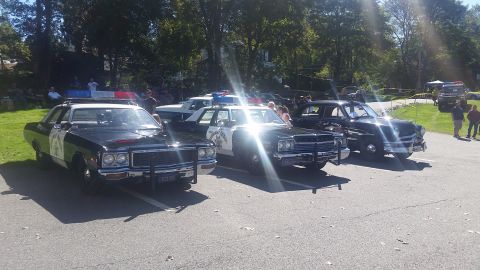 1991 Ford LTD Crown Victoria - A lineup of vintage police vehicles, including a black and white patrol car, are displayed outdoors on a sunny day.