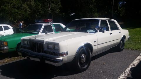 1991 Ford LTD Crown Victoria - A white sedan is parked next to a green police car.