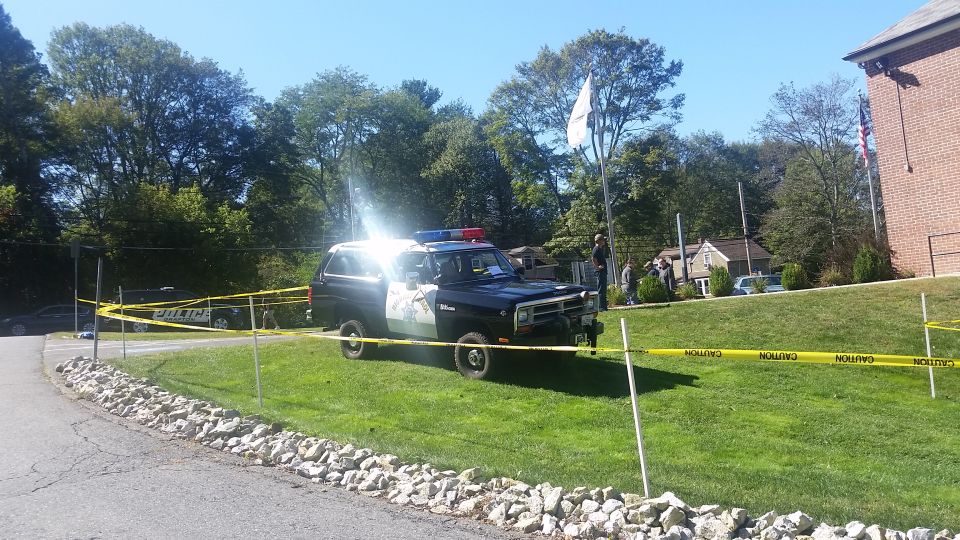 Black and white police SUV with light bar, parked on grass behind caution tape