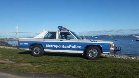 1991 Ford LTD Crown Victoria - Side view of a 1991 Ford Crown Victoria police car parked near the water under a clear blue sky.