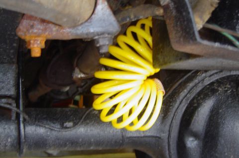 1974 Ford Bronco - Close-up of a yellow coiled hose near the suspension of a vehicle.
