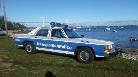 1991 Ford LTD Crown Victoria - A 1991 Ford Crown Victoria police car is parked by the water with a bridge in the background.