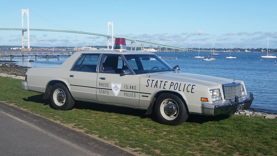 Gray police car with 'Rhode Island State Police' text, parked by the water