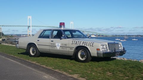 1991 Ford LTD Crown Victoria - A Rhode Island State Police car is parked by the water with a bridge in the distance.